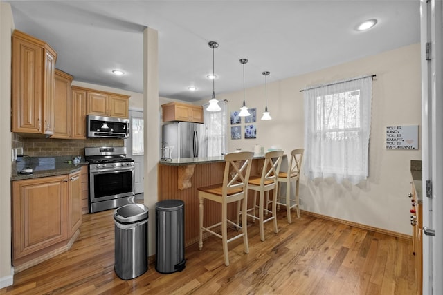 kitchen with stainless steel appliances, light wood-type flooring, a breakfast bar area, baseboards, and decorative backsplash