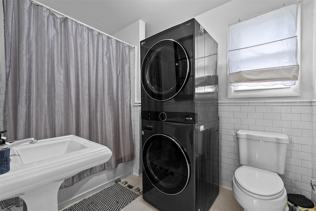 bathroom with stacked washer / drying machine, toilet, a sink, and tile walls