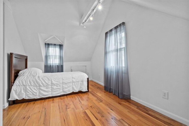 bedroom with track lighting, lofted ceiling, hardwood / wood-style floors, and baseboards