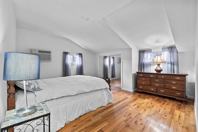 bedroom featuring lofted ceiling, light wood finished floors, baseboards, and an AC wall unit