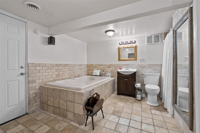 bathroom featuring tile walls, toilet, stone tile floors, a bath, and vanity