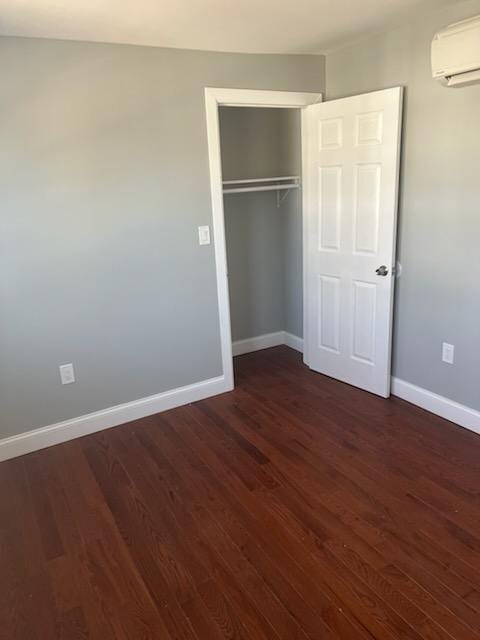 unfurnished bedroom featuring a closet, baseboards, dark wood-style floors, and a wall mounted air conditioner