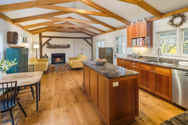 kitchen featuring a lit fireplace, stainless steel dishwasher, a sink, dark stone countertops, and vaulted ceiling with beams