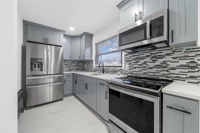 kitchen with tasteful backsplash, a sink, gray cabinetry, stainless steel appliances, and marble finish floor