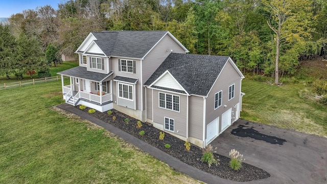 view of side of home with aphalt driveway, roof with shingles, covered porch, an attached garage, and a lawn