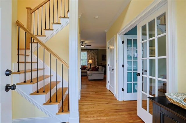stairway with ornamental molding, a ceiling fan, french doors, and wood finished floors