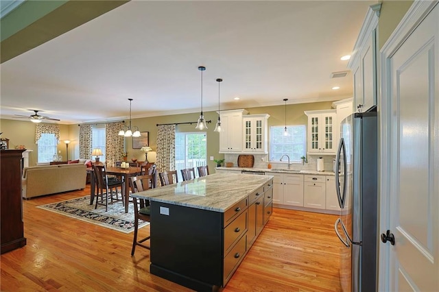 kitchen with a sink, glass insert cabinets, a kitchen bar, white cabinets, and freestanding refrigerator