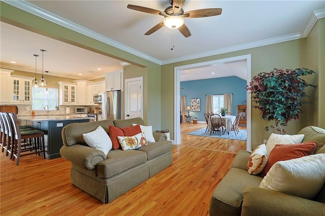 living area featuring a toaster, a ceiling fan, crown molding, baseboards, and light wood-style flooring