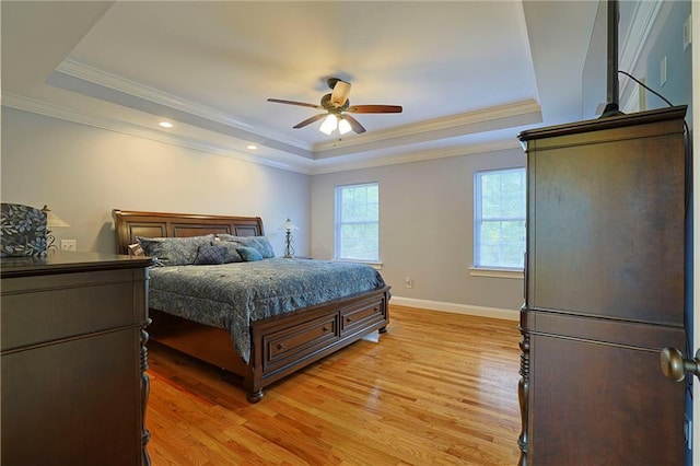 bedroom with baseboards, light wood-style floors, crown molding, and a tray ceiling