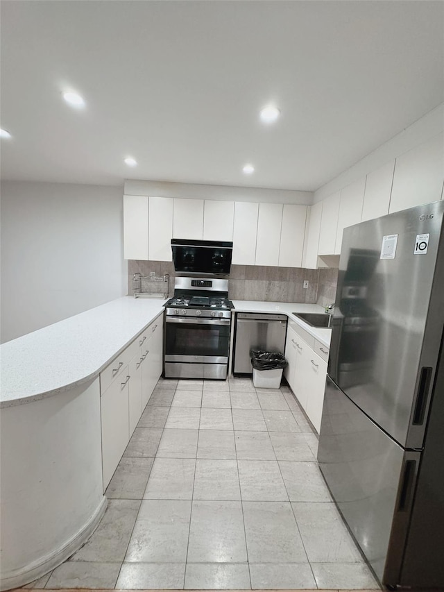 kitchen featuring white cabinets, appliances with stainless steel finishes, light countertops, a peninsula, and backsplash