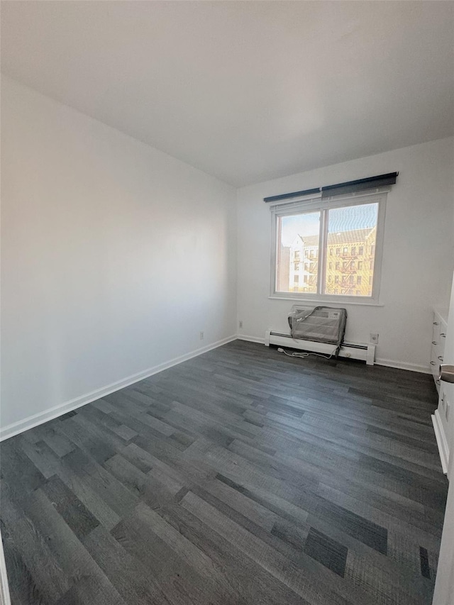 spare room with baseboards, a baseboard heating unit, and dark wood finished floors