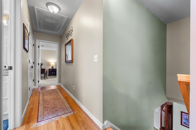 hallway featuring attic access, light wood-type flooring, and baseboards