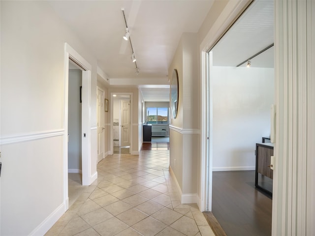corridor featuring track lighting, light tile patterned flooring, and baseboards