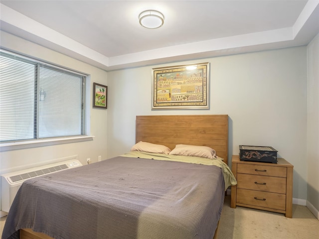 bedroom featuring baseboards, a raised ceiling, light carpet, and a wall unit AC