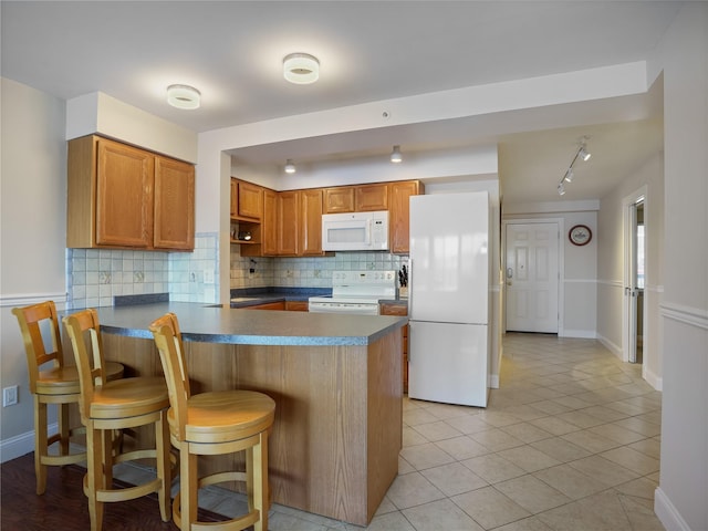 kitchen with white appliances, a peninsula, backsplash, dark countertops, and brown cabinetry