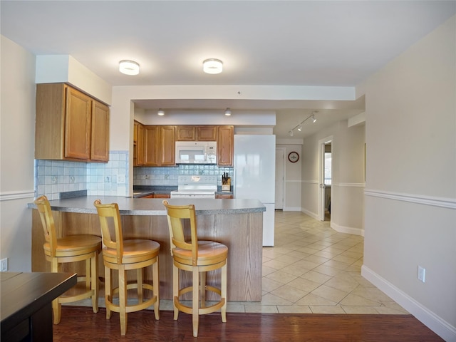 kitchen with tasteful backsplash, baseboards, white appliances, a peninsula, and brown cabinetry