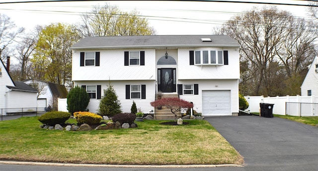 bi-level home featuring an attached garage, a front yard, fence, and driveway