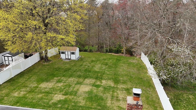 view of yard with a fenced backyard, an outbuilding, a wooded view, and a storage unit