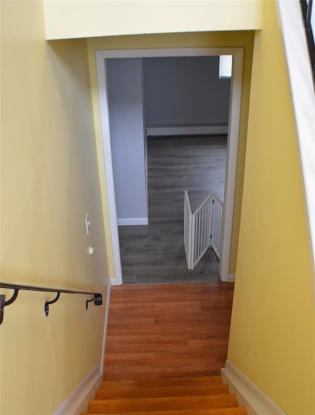 stairs with a baseboard heating unit, baseboards, and wood finished floors