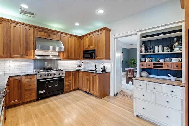 kitchen featuring under cabinet range hood, luxury range, brown cabinets, and black microwave