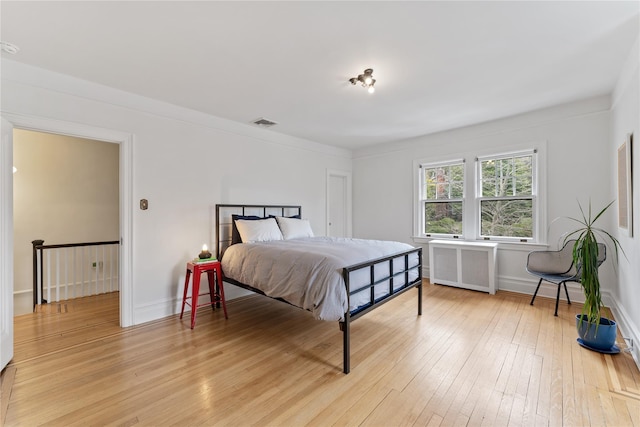 bedroom with light wood-style floors, radiator, baseboards, and visible vents