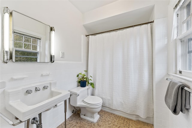 full bath with a sink, tile walls, shower / bath combo with shower curtain, and toilet