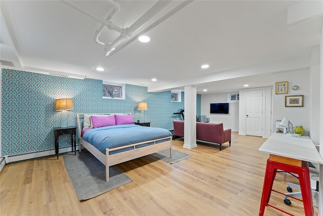 bedroom with an accent wall, a baseboard heating unit, wallpapered walls, and light wood-style flooring