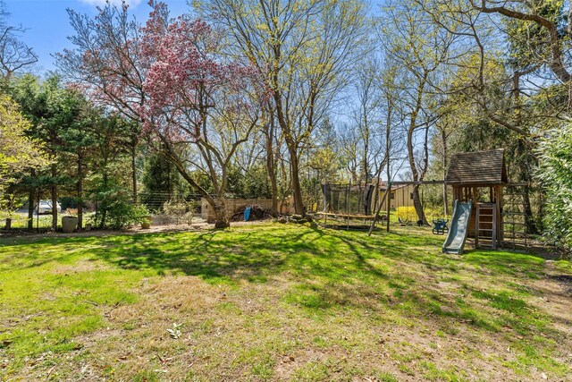 view of yard featuring fence, a trampoline, and a playground
