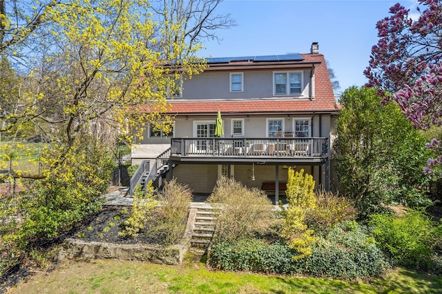 back of property featuring a chimney, solar panels, a deck, stairs, and stucco siding