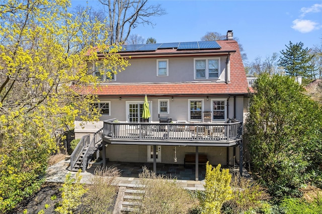 back of house featuring a wooden deck, stucco siding, a chimney, roof mounted solar panels, and stairway