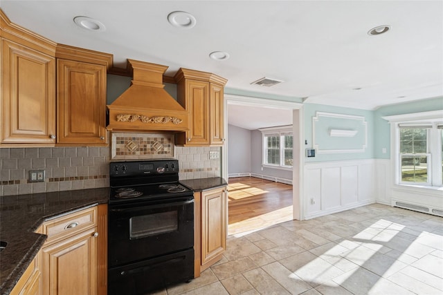 kitchen with custom exhaust hood, visible vents, tasteful backsplash, black range with electric cooktop, and a wainscoted wall