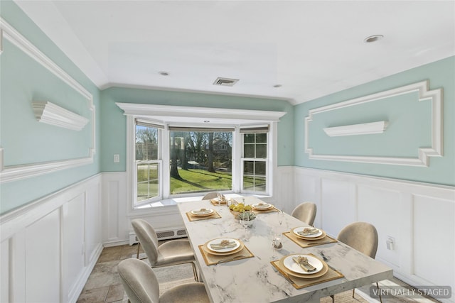 dining room with a decorative wall, stone finish floor, wainscoting, and visible vents