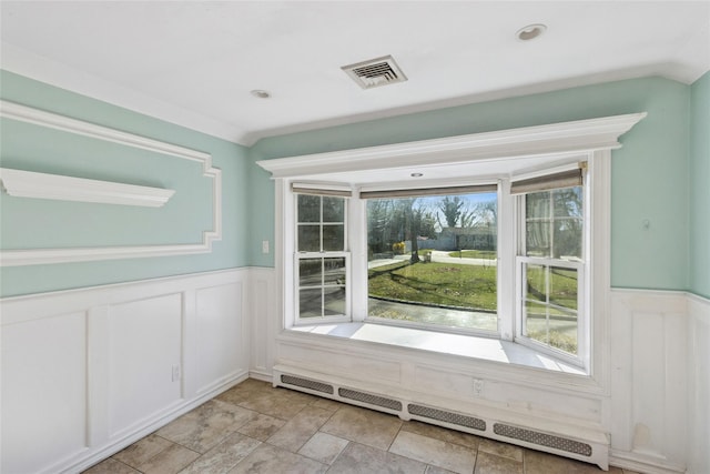 interior space with a decorative wall, a baseboard heating unit, visible vents, and a wainscoted wall