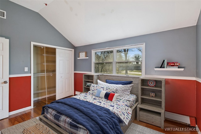 bedroom featuring a closet, visible vents, vaulted ceiling, wood finished floors, and baseboards