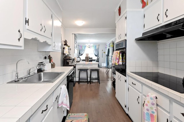 kitchen featuring black appliances, under cabinet range hood, a sink, and tile counters
