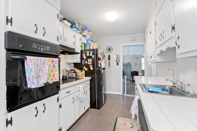 kitchen featuring a sink, under cabinet range hood, black appliances, backsplash, and tile countertops