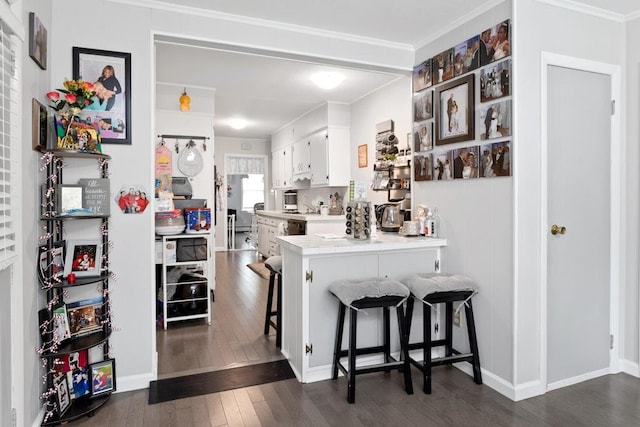 kitchen with ornamental molding, white cabinets, a kitchen breakfast bar, and dark wood finished floors
