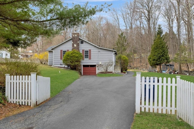 view of front facade with a front yard, a garage, a chimney, fence, and driveway