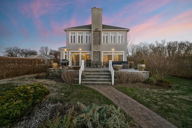 54985 Cr48, Southold, NY 11971 - back of house at dusk with an outdoor hangout area, a yard, stucco siding, stone siding, and a chimney