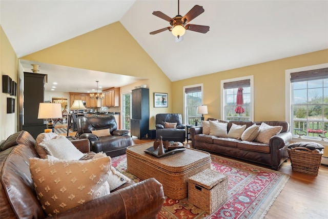 living room featuring light wood-type flooring, a wealth of natural light, high vaulted ceiling, and ceiling fan with notable chandelier
