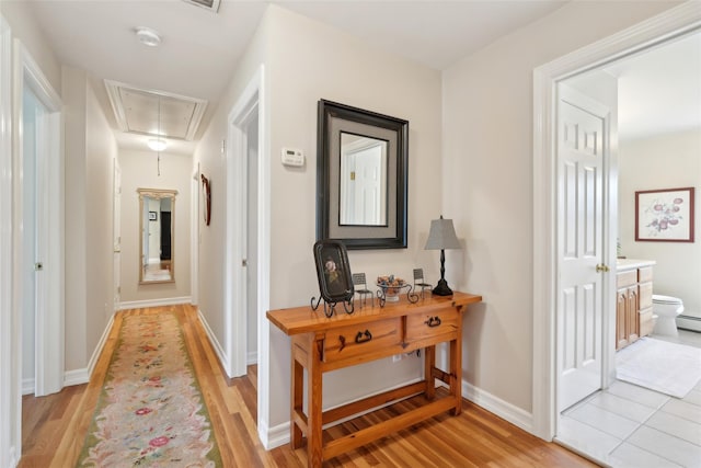 hall featuring attic access, light wood-style flooring, and baseboards