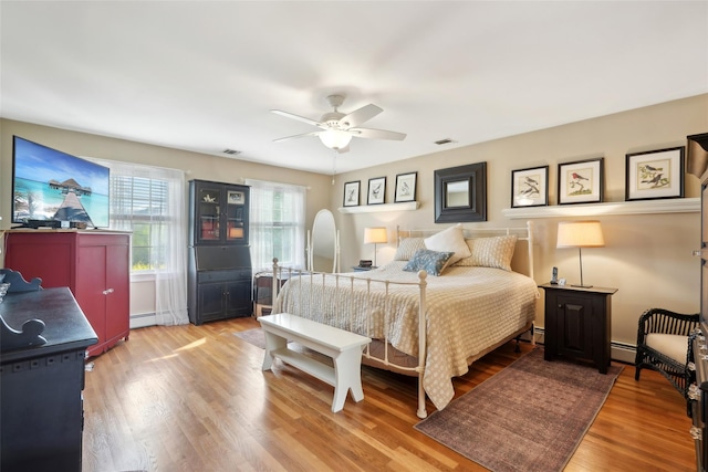 bedroom with a baseboard radiator, a ceiling fan, wood finished floors, and visible vents