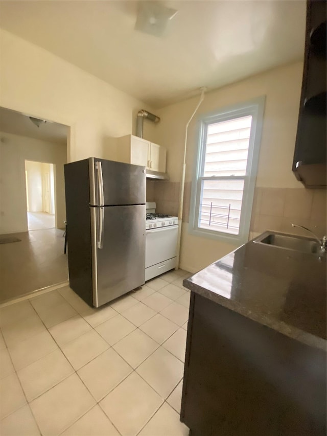 kitchen featuring freestanding refrigerator, light tile patterned floors, white cabinetry, white range with gas stovetop, and a sink