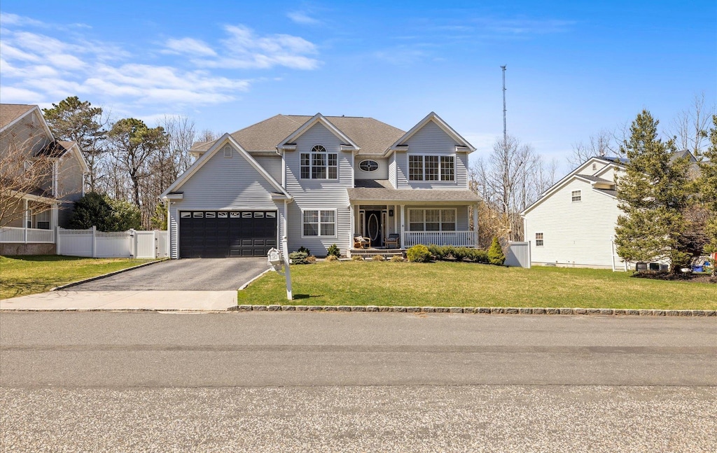 traditional-style home featuring driveway, a front lawn, a porch, a garage, and fence
