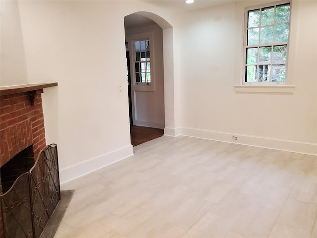 unfurnished living room with arched walkways, baseboards, a brick fireplace, and recessed lighting