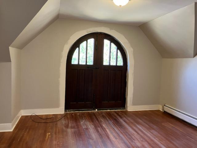 foyer entrance featuring baseboards, arched walkways, baseboard heating, wood finished floors, and lofted ceiling