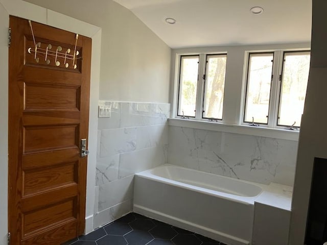 bathroom with recessed lighting, tile patterned floors, a bath, lofted ceiling, and tile walls