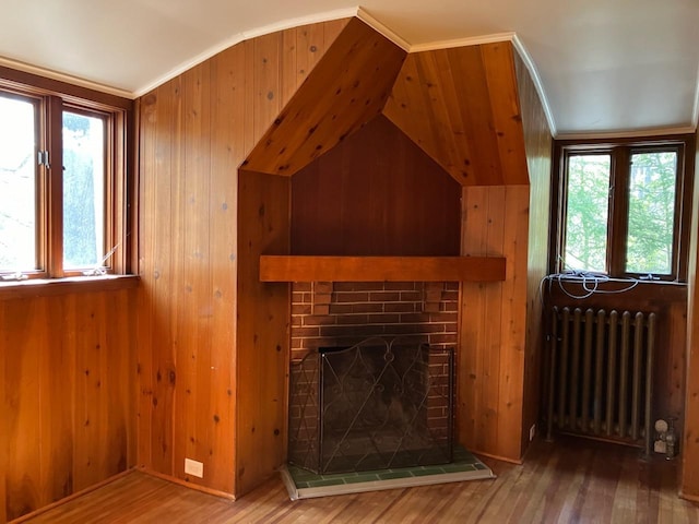 unfurnished living room featuring wood walls, radiator heating unit, vaulted ceiling, and wood finished floors