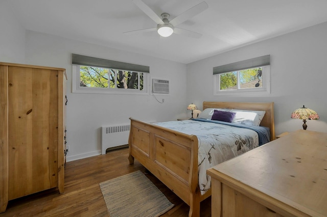 bedroom featuring radiator heating unit, a ceiling fan, baseboards, wood finished floors, and a wall mounted AC