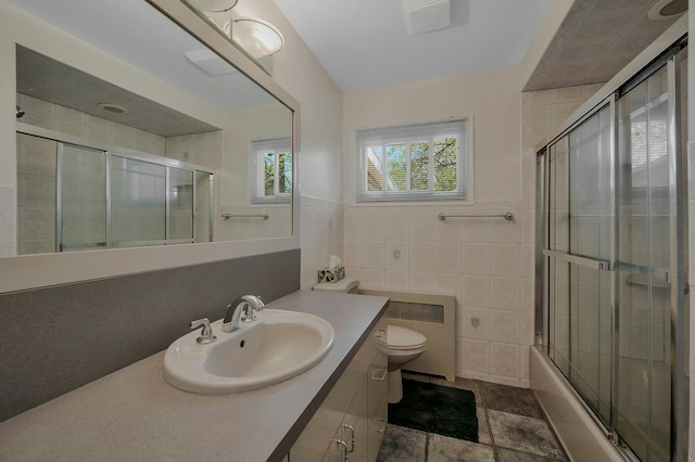 full bath featuring vanity, combined bath / shower with glass door, toilet, and tile walls
